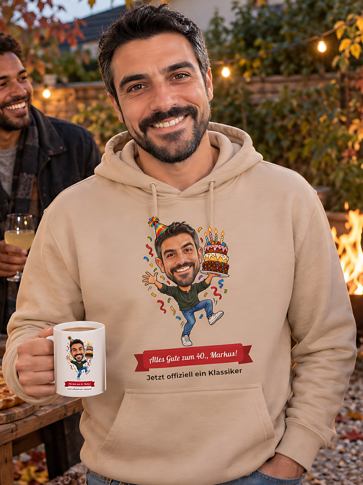 Geburtstagsfeier im herbstlichen Garten mit Feuerschale: Markus trägt einen sandfarbenen Hoodie mit seiner Karikatur und hält eine Tasse mit demselben Motiv, Freunde stoßen mit Federweißer an